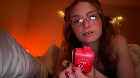 Media: A video of a pale, young woman with curly brown hair, wearing glasses, holding a red spray can in a dimly lit room.