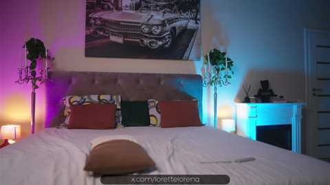 Media: Video of a modern bedroom with a plush, beige tufted headboard, colorful pillows, and a vintage car poster. Ambient lighting highlights potted plants, a white dresser, and a cozy, dimly lit corner.