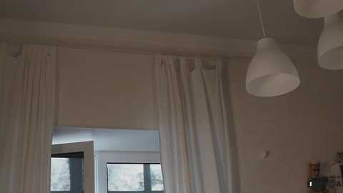 Media: Video of a modern room with white curtains, a large window, and a white pendant lamp hanging from the ceiling. The room has a minimalist, clean aesthetic.