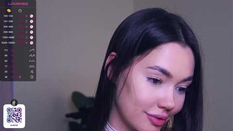 Media: Video of a smiling Asian woman with straight black hair and light skin, wearing a white blouse, in a dimly lit room with a blurred background.