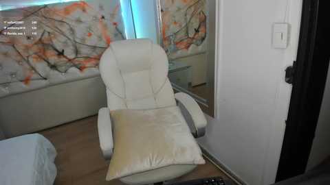 Media: A video of a minimalist living room with a white leather recliner, beige throw pillow, wooden floor, floral-patterned wall, and a partially open white door.