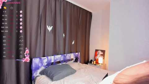 Media: Video of a cozy, modern bedroom with a purple and gray bedding setup, dark curtains, and a lit lamp on a nightstand.