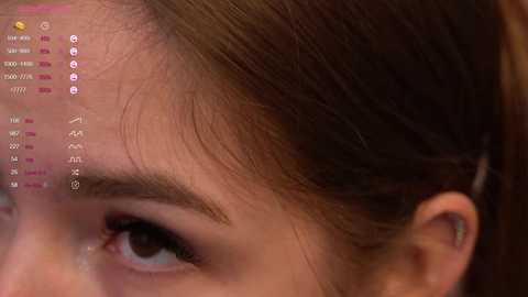 Media: Close-up video of a woman's face, focusing on her right eye and eyebrow. The background is blurred, highlighting the skin texture and subtle makeup. Digital icons and text overlayed on the image suggest a virtual reality or augmented reality experience.