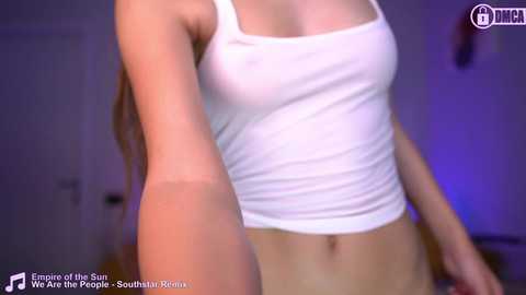 Media: Video of a slender, light-skinned woman with small breasts, wearing a tight white tank top, in a dimly lit room.