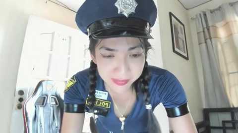 Media: Video of a young Asian woman in a blue police uniform with braided hair, wearing a hat, ID badge, and handcuffs.