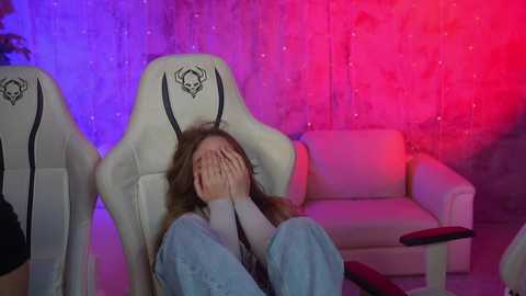 Media: A video of a woman sitting in a white gaming chair, covering her face with her hands, against a colorful backdrop with purple and red lights.