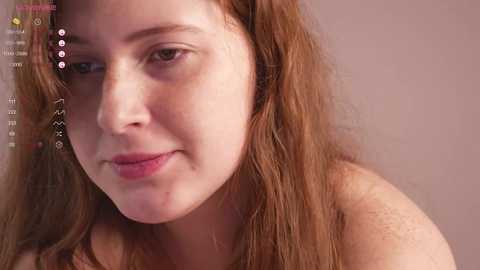 Media: Video of a fair-skinned, freckled woman with long, wavy red hair and light makeup, smiling slightly, against a neutral background, with a virtual chat interface overlay.