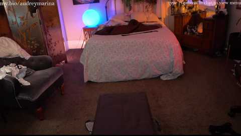 Media: A dimly lit bedroom with a messy bed, a large round blue lamp, and a dark curtain. Clothes scattered on the floor and furniture. URL watermark in the top corners.