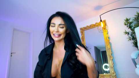 Media: Video of a smiling, dark-haired woman in a black blouse, with a large, ornate gold-framed mirror in the background.