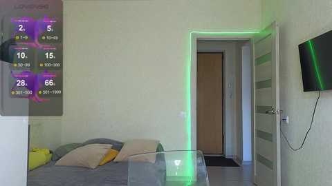 Media: Video of a modern, minimalist bedroom with a single bed, gray bedding, and a closed wooden door. A digital display in the corner shows a game score.