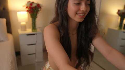 Media: A video of a young, smiling woman with long, dark hair, topless, in a cozy room with white furniture, a lamp, and flowers.