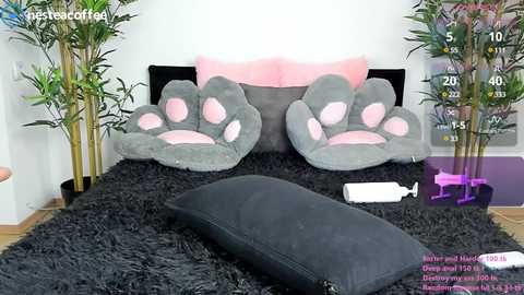 Media: Video of a cozy bedroom with a black shag rug, gray paw-print pillows, pink accents, bamboo plants, and a black pillow.