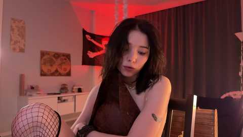 Media: A video of a young Asian woman with dark hair, wearing a brown dress and fishnet stockings, sitting in a dimly lit room with red lighting.