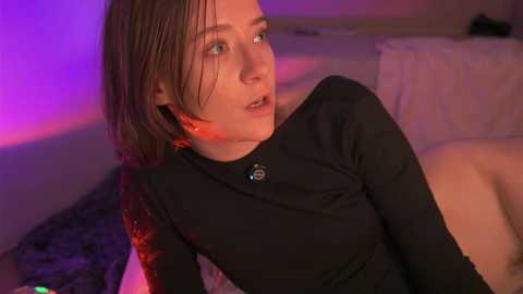 Media: Video of a young woman with short, wet hair, wearing a black top, lying on a bed with a purple light.