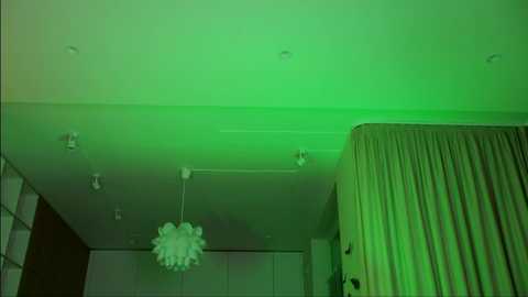 Media: Video of a modern room with a greenish glow, featuring a chandelier, beige curtains, and recessed lighting on the ceiling.