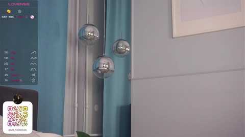 Media: Video of a modern bedroom with a teal wall, grey headboard, and two metallic pendant lights hanging from the ceiling. A framed picture hangs on the right wall.