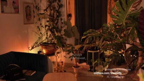 Media: Video of a cozy indoor living room with warm lighting, featuring a green sofa, potted plants, and a framed picture on a beige wall.