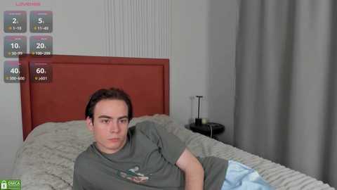 Media: Video of a young man with short dark hair, wearing a gray t-shirt, lying on a bed with beige sheets and a red headboard. A virtual overlay displays health stats, including calories and steps.