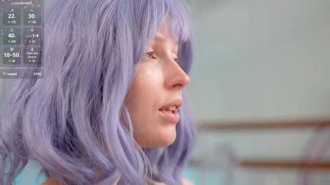 Media: Video of a light-skinned person with shoulder-length, wavy lavender hair, wearing a white top, viewed from the side, in a blurred outdoor setting.