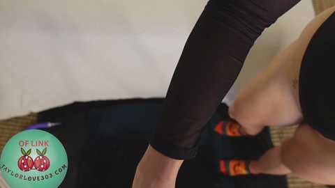 Media: A video of a person in black leggings and socks, bending over to put on a black jacket, with a teal logo in the background.