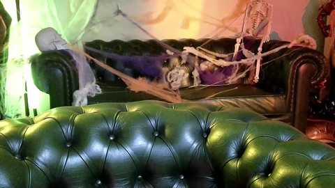 Media: A video of a vintage green leather tufted sofa with a macabre Halloween theme, featuring a spider web, a skeleton, and a hanging chair with a ghostly figure.