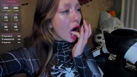 Media: Video of a young woman in a Spider-Man costume, looking shocked and biting her finger, surrounded by a cluttered room with a skull hat and a Spider-Man backpack.