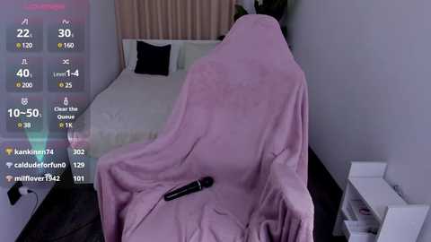 Media: A video of a neatly made bed with a pink blanket partially covering a black vibrator on the pillow. The room is minimalist with beige walls and a white nightstand.