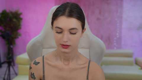 Media: Video of a young woman with fair skin, brown hair in a bun, wearing a white veil and black lace dress. She has a serene expression, seated in a white gaming chair with a pink backdrop.