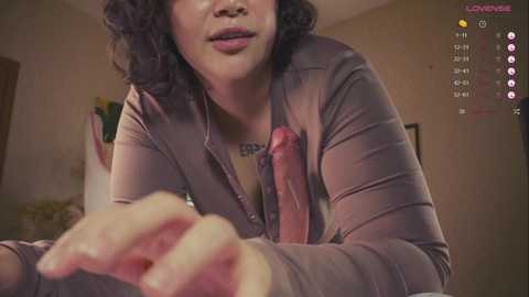 Media: A video of a woman with curly hair and a brown cardigan, leaning forward, displaying a circumcised penis. Background shows a dimly lit room with a clock displaying 20:47.