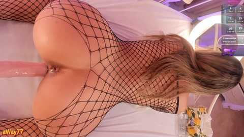 Media: Video of a blonde woman in black fishnet lingerie, bent over with her buttocks exposed, a large dildo penetrating her anus, in a medical room with white walls and a blue ceiling.