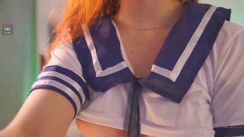 Media: Video of a woman with fair skin, wearing a white and navy blue Japanese schoolgirl sailor uniform with a low-cut neckline, showing cleavage. Background is blurred.