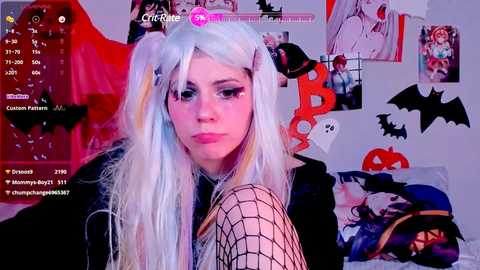 Media: Video of a pale-skinned woman with long, pastel-colored hair in a Halloween costume, wearing fishnet stockings, in a cluttered, Halloween-themed room.