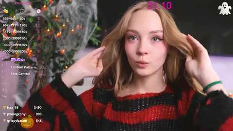 Media: Video of a young woman with fair skin, blonde hair, and a red and black striped sweater, adjusting her hair in a festive room with a lit Christmas tree and streaming overlays.