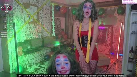 Media: Video of a woman with curly green hair, wearing a red dress, clown makeup, and yellow scarf, in a dimly-lit room with psychedelic lighting and graffiti walls.