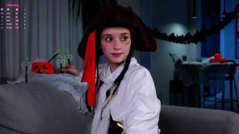 Media: A video of a young girl in a pirate costume with a red and black hat, white shirt, and gray couch in a dimly lit, Halloween-themed room.