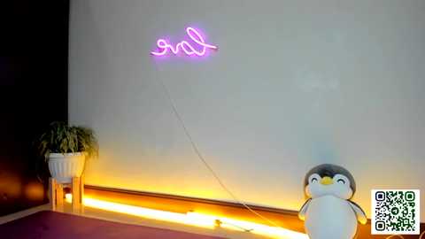 Media: Video of a dimly lit room featuring a glowing neon \"smile\" sign on a white wall, a penguin toy, and a potted plant on the floor.