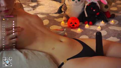 Media: Video of a topless, slender woman with small breasts wearing black thong, lying on a bed with Halloween decorations, including a pumpkin.