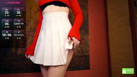 Media: Video of a woman in a red crop top and high-waisted white skirt, lifting the skirt to reveal her black underwear, in a modern room with a red wall and abstract art.