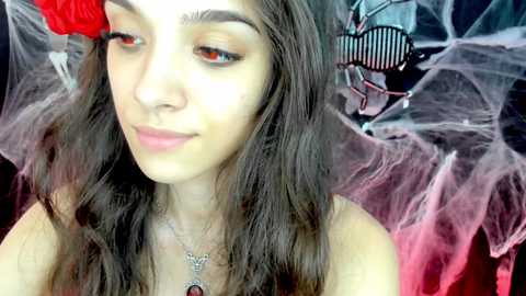 Media: Video of a young woman with long, dark hair, wearing a red flower and butterfly wings, with a soft-focus background.