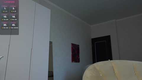 Media: Video of a dimly lit, minimalist bedroom with a beige armchair, white walls, and a digital clock displaying 1:17. A red abstract painting and a dark wooden door are visible.