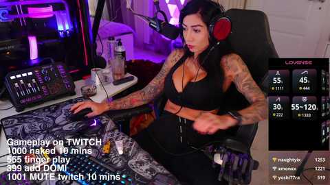 Media: A video of a tattooed, dark-haired woman with large breasts, wearing a black sports bra and headphones, playing a Twitch stream, surrounded by gaming equipment.