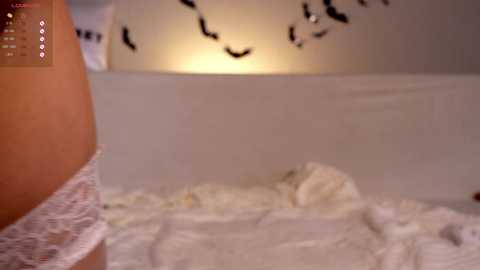 Media: Video of a woman in white lace lingerie lying on a bed with a Halloween-themed wall behind her, featuring black bats and a glowing light.