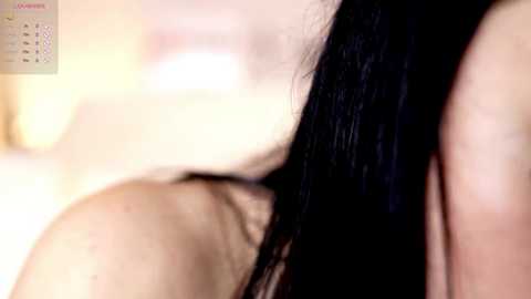 Media: A close-up video shows a person's shoulder and black hair, blurred background, likely taken indoors with soft lighting.