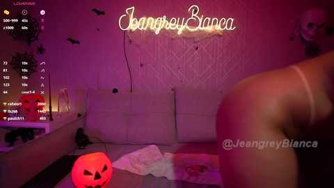 Media: Video of a dimly-lit, cozy room with a \"JenagreyBlanca\" watermark, featuring a glowing neon sign reading \"JenagreyBianca,\" a large pumpkin, and a black cat.