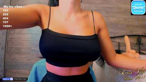 Media: Video of a woman with fair skin wearing a black sports bra and high-waisted black pants, standing in a bedroom with wooden walls and a bed.