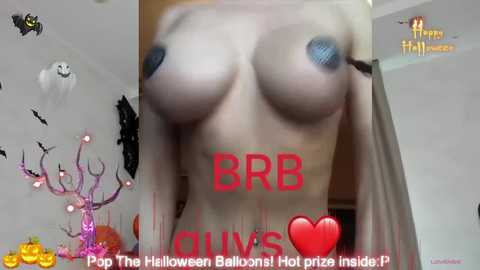 Media: Video of a woman with large breasts and blue nipple pasties, wearing a white shirt. Halloween decorations including a jack-o'-lantern and a ghost in the background. Text overlay: \"BRB, The Halloween Balloons! Hold Piz! \ud83d\udc95\