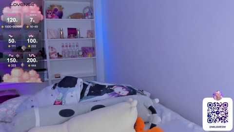 Media: Video of a cozy bedroom with a white bed featuring a plush pillow and a polka-dotted blanket. A white shelving unit in the background holds various cosmetics and a pink teddy bear. The room has a soft, pastel color scheme.