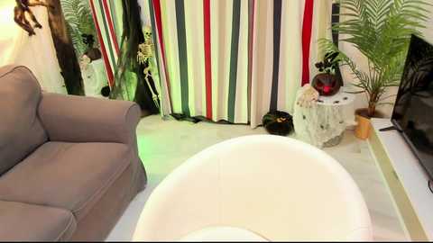 Media: Video of a cozy living room with a gray couch, white coffee table, colorful striped curtains, potted plants, and a black handbag on the floor.