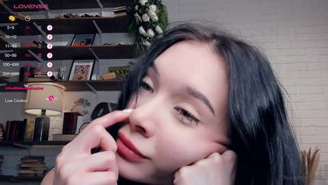 Media: A video of a young Asian woman with long black hair, resting her head on her hand, smiling, in a cozy bookshelf-filled room.