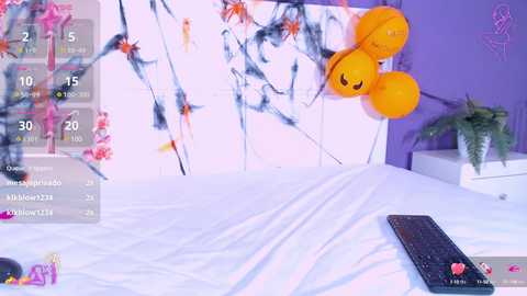 Media: Video of a modern bedroom with a purple wall, white bed, and a black keyboard on the bed. Two smiling yellow plushies hang on a white wall, and a green fern sits on a white shelf.